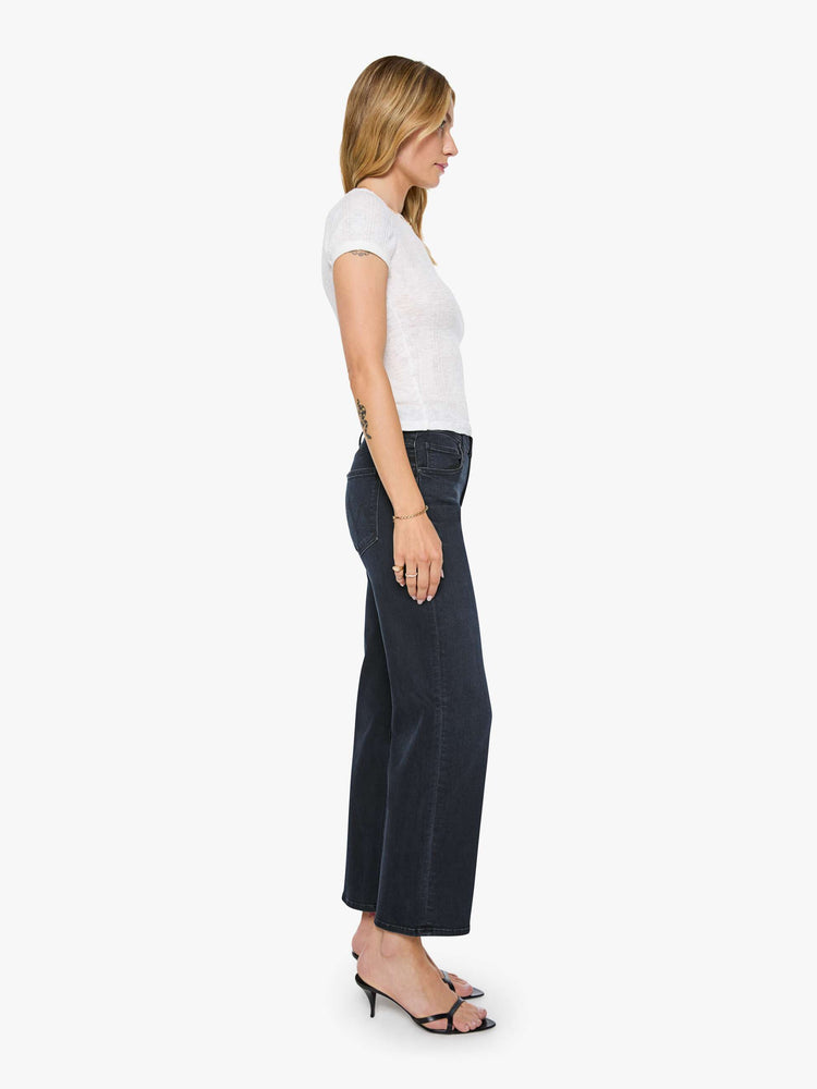 Side view of a woman in a dark denim mid-rise jean with a wide straight leg, zip fly and clean ankle-length inseam. 