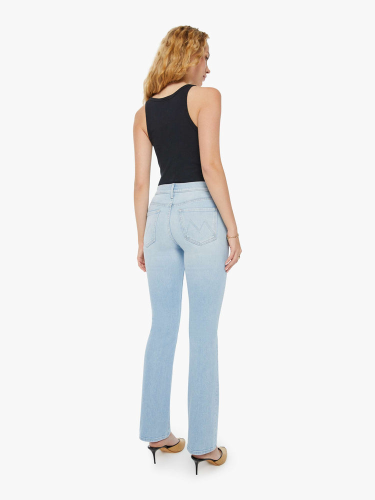 Back view of a woman in a high-rise light blue bootcut jean with whiskering and fading. Paired with a black tank top and mules.