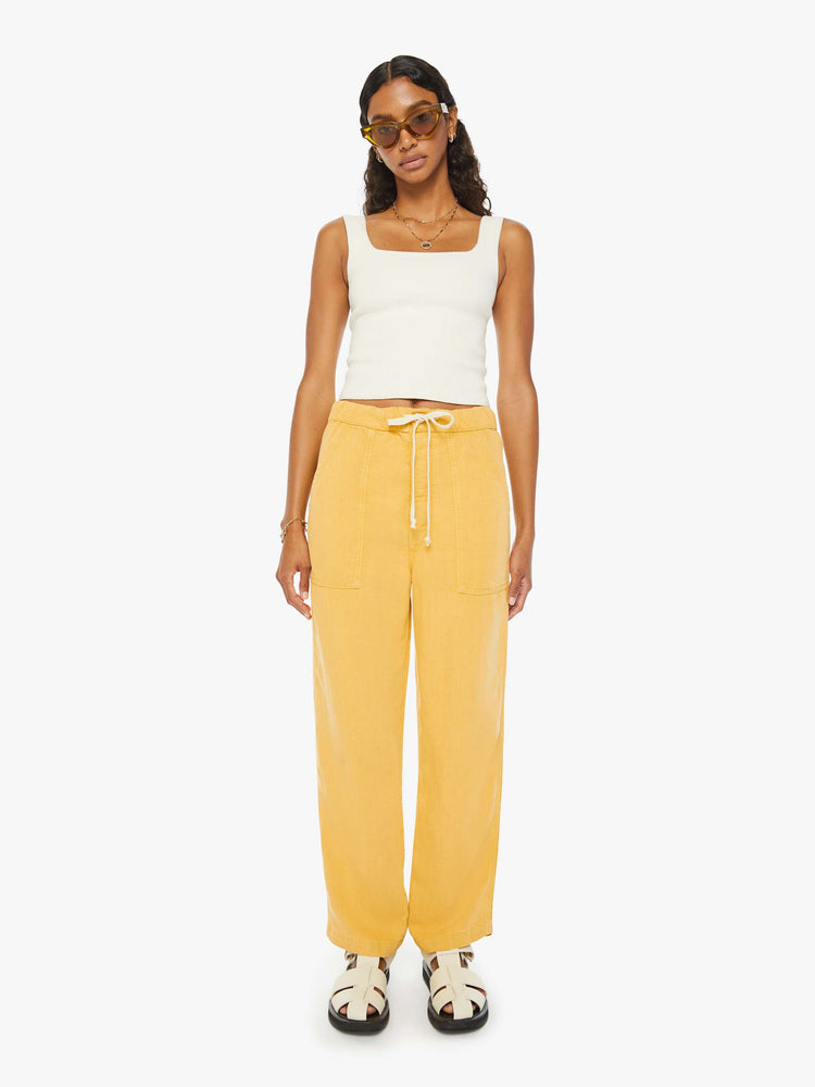 Front view of a woman in super high-waisted sunny yellow pants with wide straight leg, an elastic drawstring waistband, button fly, oversized patch pockets and an ankle-length inseam.