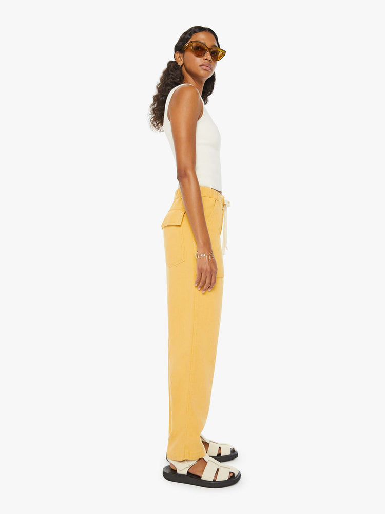 Side view of a woman in super high-waisted sunny yellow pants with wide straight leg, an elastic drawstring waistband, button fly, oversized patch pockets and an ankle-length inseam.