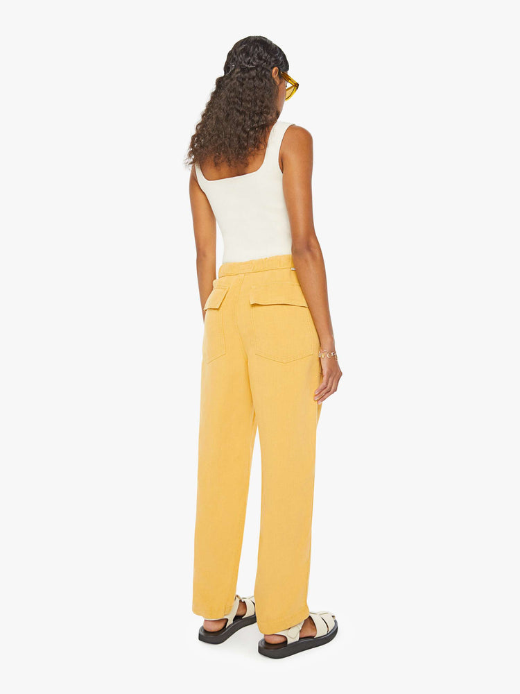 Back view of a woman in super high-waisted sunny yellow pants with wide straight leg, an elastic drawstring waistband, button fly, oversized patch pockets and an ankle-length inseam.