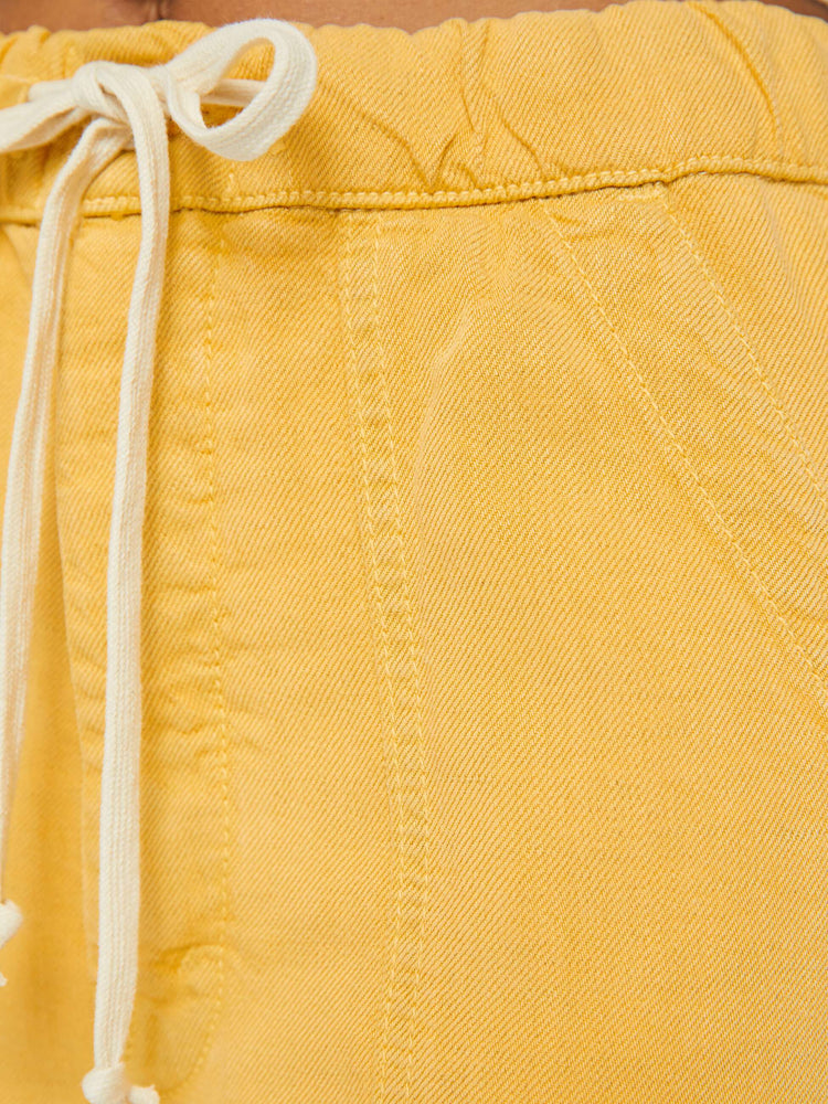 Detailed view of a woman in super high-waisted sunny yellow pants with wide straight leg, an elastic drawstring waistband, button fly, oversized patch pockets and an ankle-length inseam.