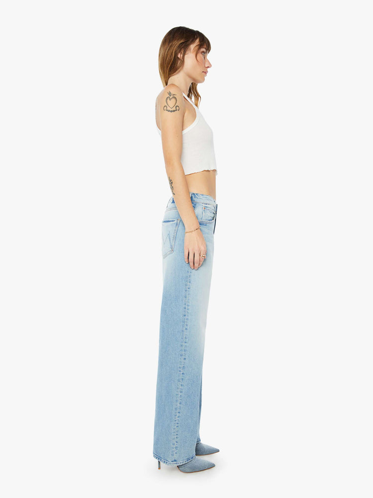 Side view of a womens light blue wash jean featuring a slouchy low rise fit, wide straight legs, and a long clean hem.