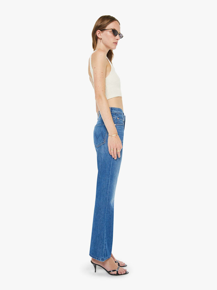 Side view of a woman in a mid blue designed to sit on the hips with a slouchy fit, these jeans feature a flared leg, zip fly, ankle-length inseam and a super high rise with a slightly dropped crotch.