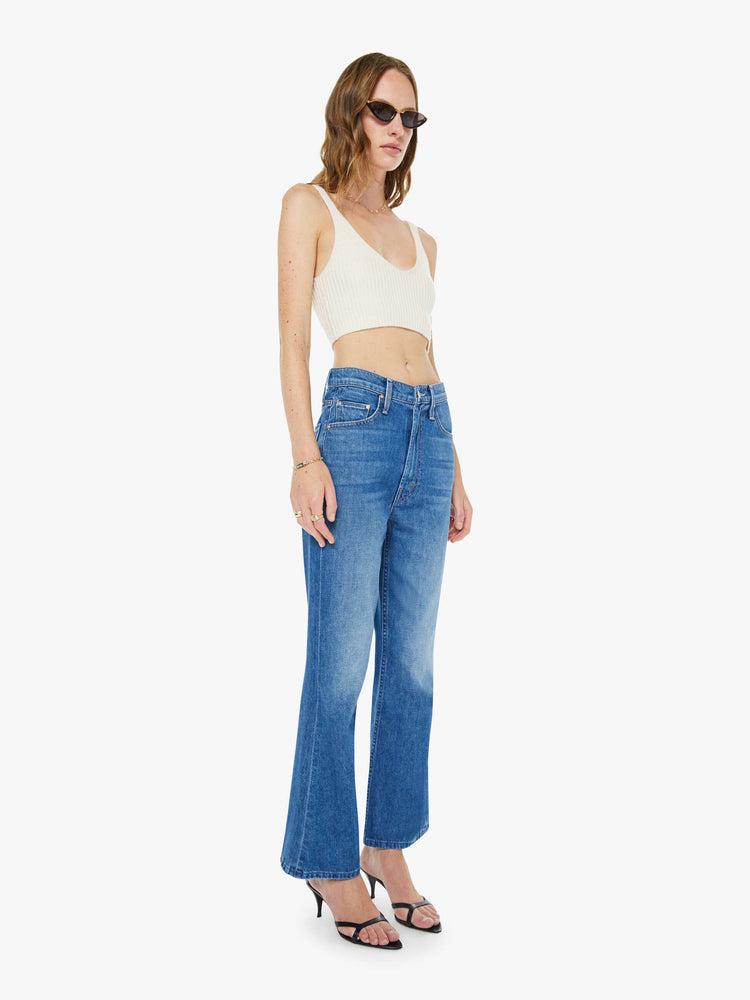 Side angle view of a woman in a mid blue designed to sit on the hips with a slouchy fit, these jeans feature a flared leg, zip fly, ankle-length inseam and a super high rise with a slightly dropped crotch.