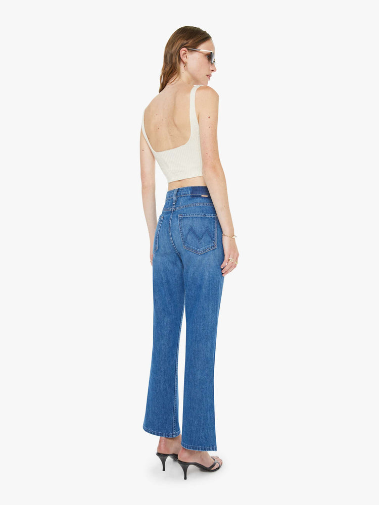Back view of a woman in a mid blue designed to sit on the hips with a slouchy fit, these jeans feature a flared leg, zip fly, ankle-length inseam and a super high rise with a slightly dropped crotch.