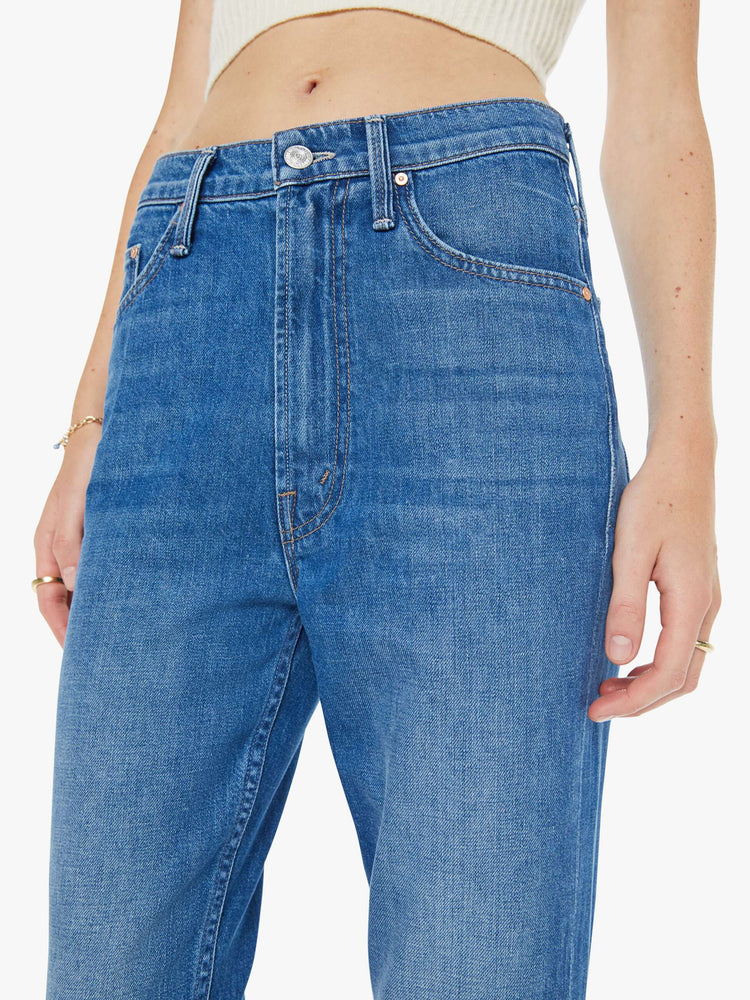 Close up view of a woman in a mid blue designed to sit on the hips with a slouchy fit, these jeans feature a flared leg, zip fly, ankle-length inseam and a super high rise with a slightly dropped crotch.