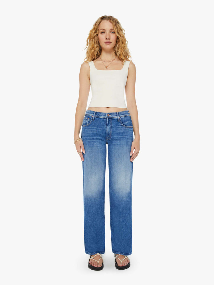 Front view of a woman in mid-blue wide leg jeans with whiskering and fading at the knees. Styled with a white tank top.