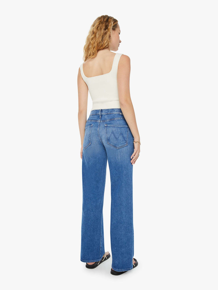 Back view of a woman in mid-blue wide leg jeans with whiskering and fading at the knees. Styled with a white tank top.