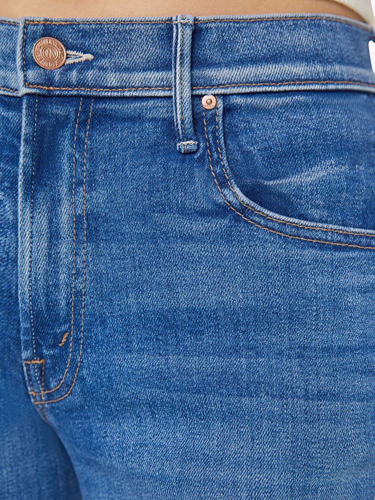 Detailed view of a woman in mid-blue wide leg jeans with whiskering and fading at the knees. Styled with a white tank top.
