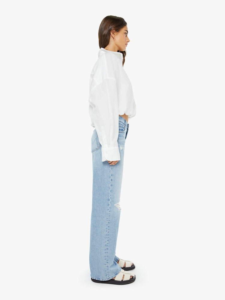 Side view of a woman in a light blue mid-rise jeans with a loose fit, zip fly, wide leg and 32-inch inseam with a clean hem.