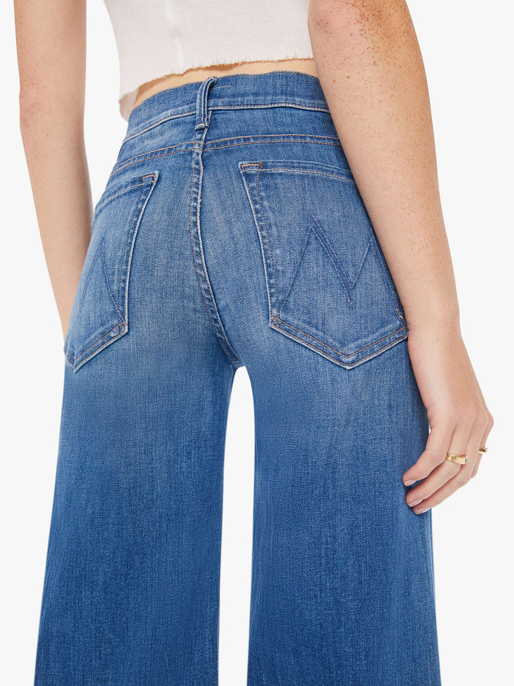 Back close up view of a woman wearing a medium blue wash jean featuring a low rise and a wide flare leg.