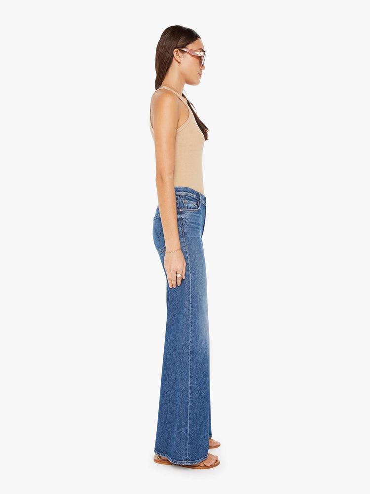 Side view of a medium blue wash jean featuring a high rise and a wide leg flare.