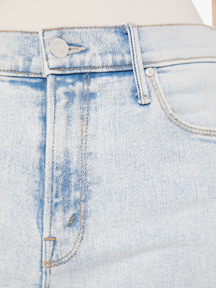 A close up detail swatch view of a light blue wash jean featuring darker blue hues around the seams, white hardware, and contrast brown thread.