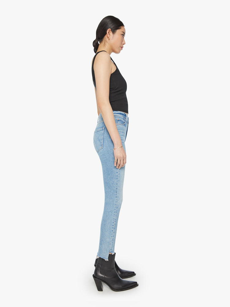 Side view of a woman mid-rise jean has a straight leg with an ankle-length inseam and a frayed step hem in a light blue wash.