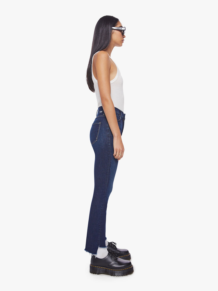 Side view of a dark blue mid-rise jean has a straight leg with an ankle-length inseam and a frayed step hem.
