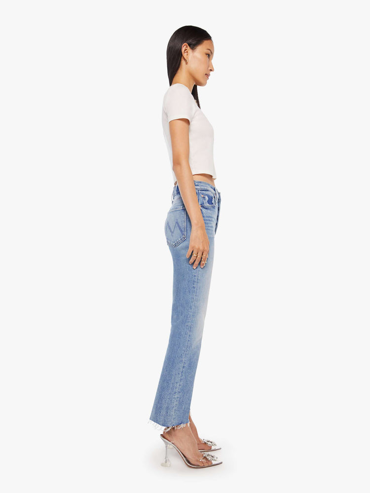 Side view of a womens high rise medium blue wash jean with a flare leg, frayed hem and fading at the knees.