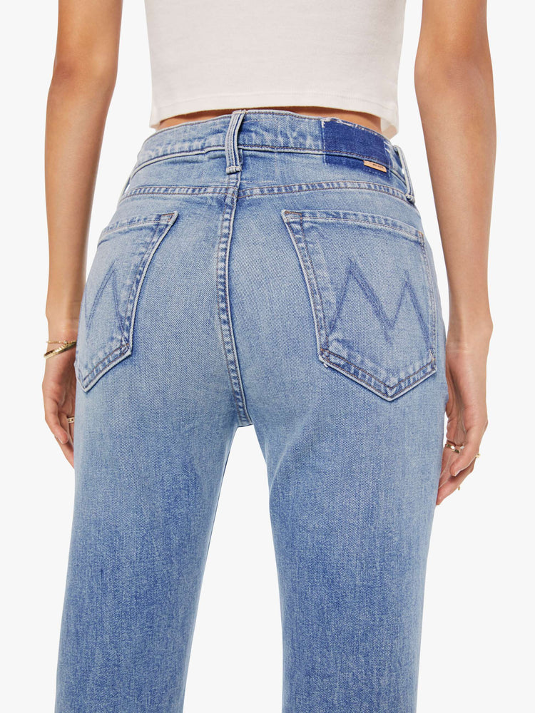 Close up view of a womens high rise medium blue wash jean with a flare leg, frayed hem and fading at the knees.