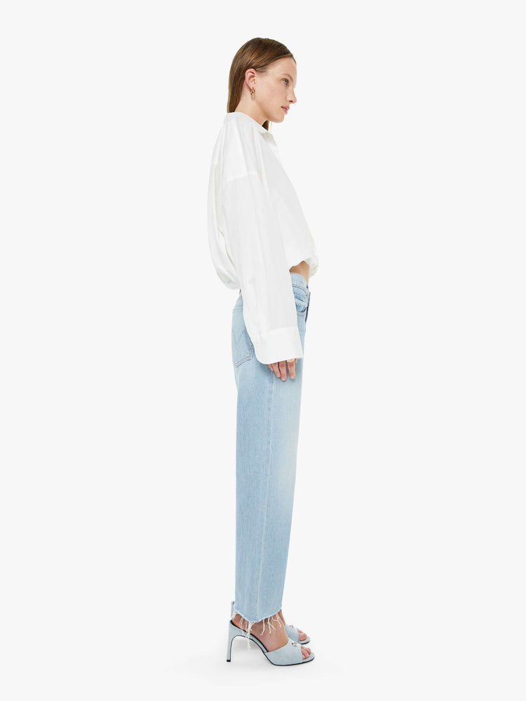 Side view of a woman in a light blue mid-rise jeans with a wide straight leg, zip fly and frayed ankle-length inseam.