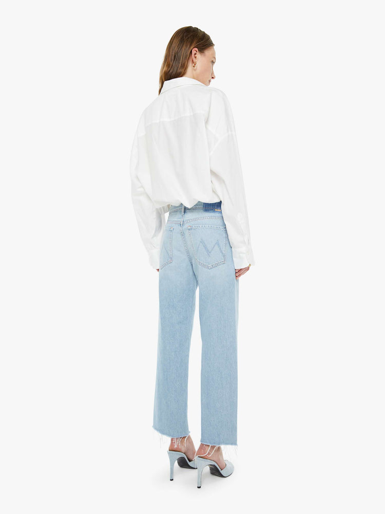 Back view of a woman in a light blue mid-rise jeans with a wide straight leg, zip fly and frayed ankle-length inseam.