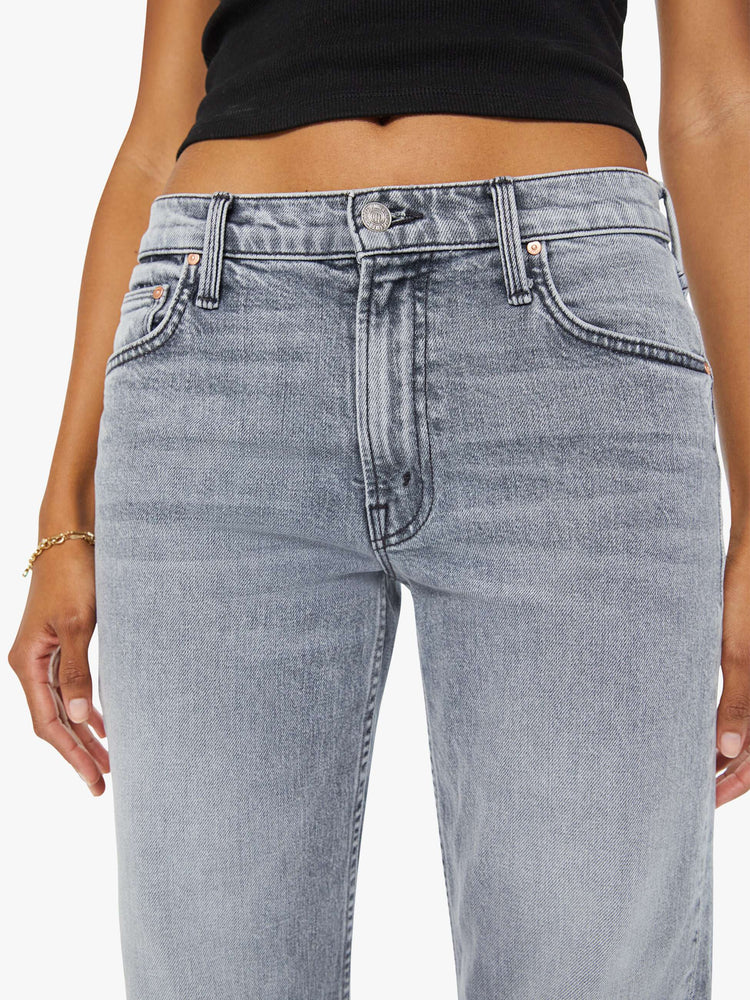 Detailed front view of a woman in light-grey high-waisted wide bootcut jeans designed to sit lower on the waist with whiskering and fading