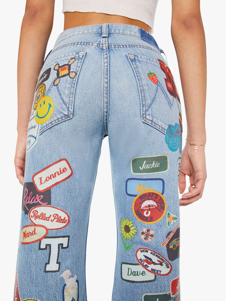 Back close up view of a woman in a light blue and colorful vinyl patches thoughout high-rise bootcut jean with a zip fly, looser leg and a 32-inch inseam with a clean hem. 