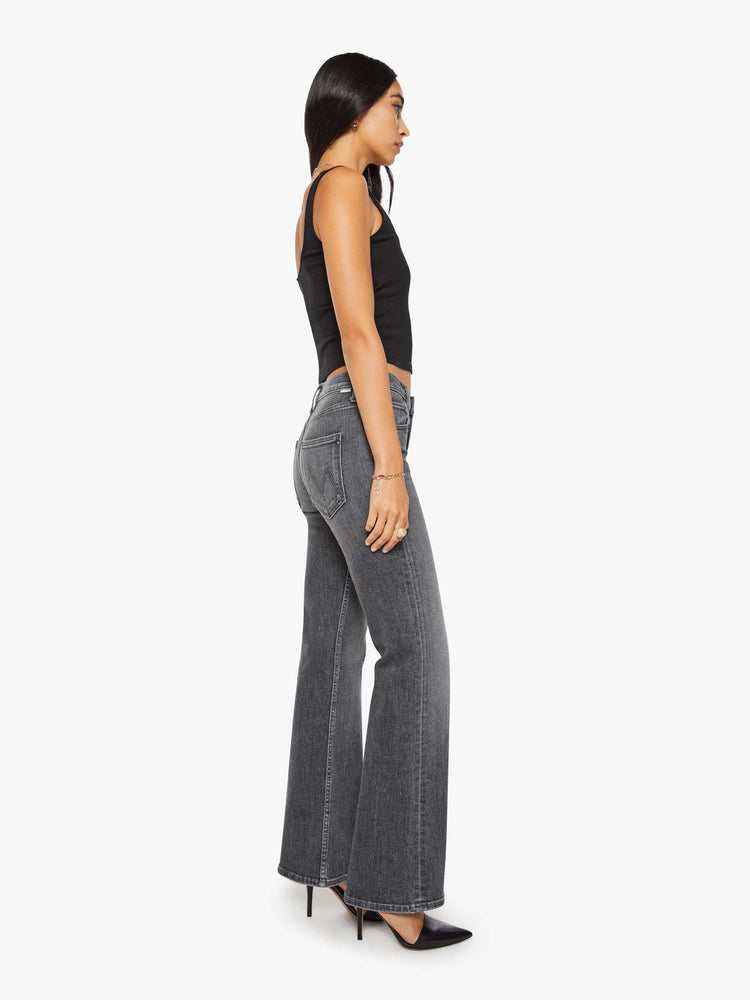 Side view of a woman in a dark grey mid-rise bootcut with a zip fly, looser leg and a long 32-inch inseam with a clean hem.