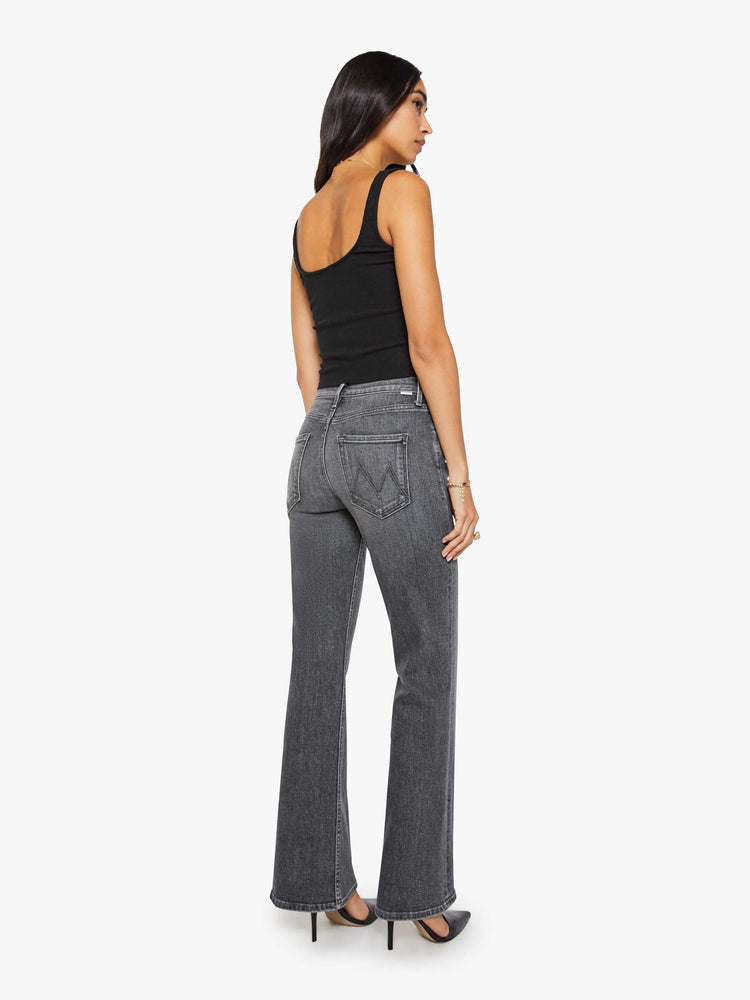 Back view of a woman in a dark grey mid-rise bootcut with a zip fly, looser leg and a long 32-inch inseam with a clean hem.