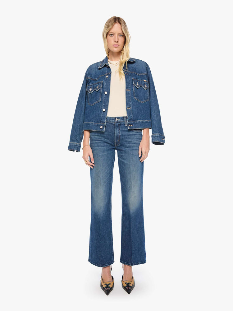 Front view of a woman in mid-blue mid-rise bootcut with a zip fly, looser leg and a long 32-inch inseam with a clean hem.
