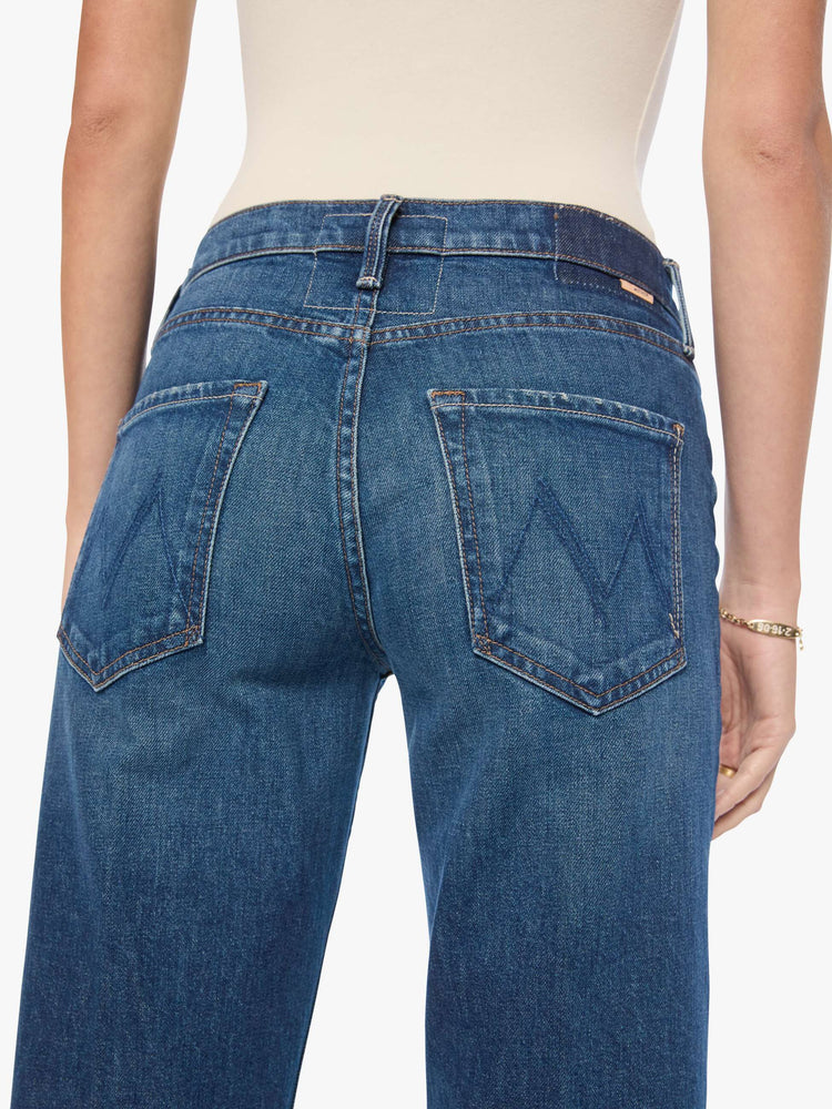 Close up view of a woman in mid-blue mid-rise bootcut with a zip fly, looser leg and a long 32-inch inseam with a clean hem.
