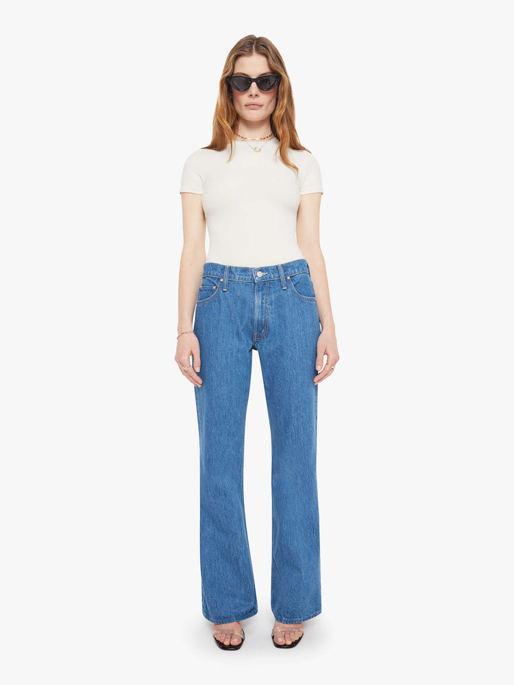 Front view of a woman in med blue high-rise bootcut with a zip fly, looser leg and a long 32-inch inseam with a clean hem.