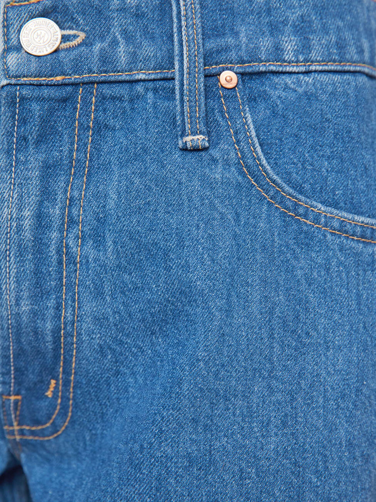 Swatch view of a woman in med blue high-rise bootcut with a zip fly, looser leg and a long 32-inch inseam with a clean hem.