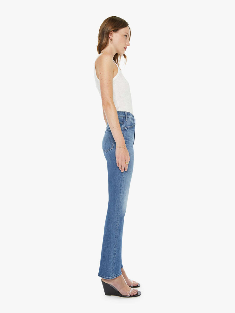 Side view of a woman in a mid blue high-rise flare has a zip fly, 28.25-inch inseam and a clean hem.