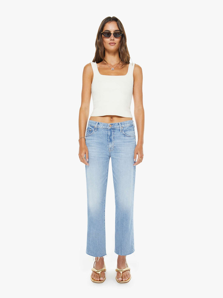Front view of a woman in a light blue mid-rise jeans with a wide straight leg, zip fly and an ankle-length inseam with a frayed hem.
