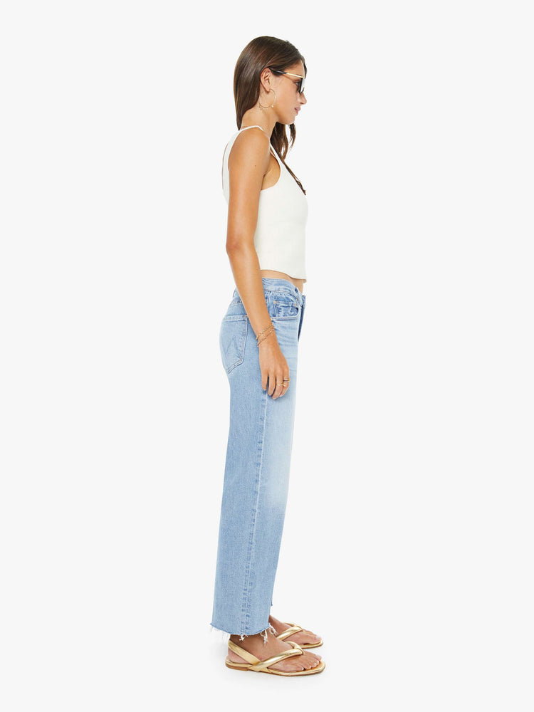 Side view of a woman in a light blue mid-rise jeans with a wide straight leg, zip fly and an ankle-length inseam with a frayed hem.