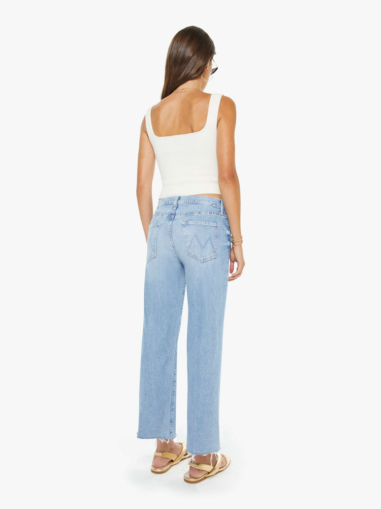 Back view of a woman in a light blue mid-rise jeans with a wide straight leg, zip fly and an ankle-length inseam with a frayed hem.