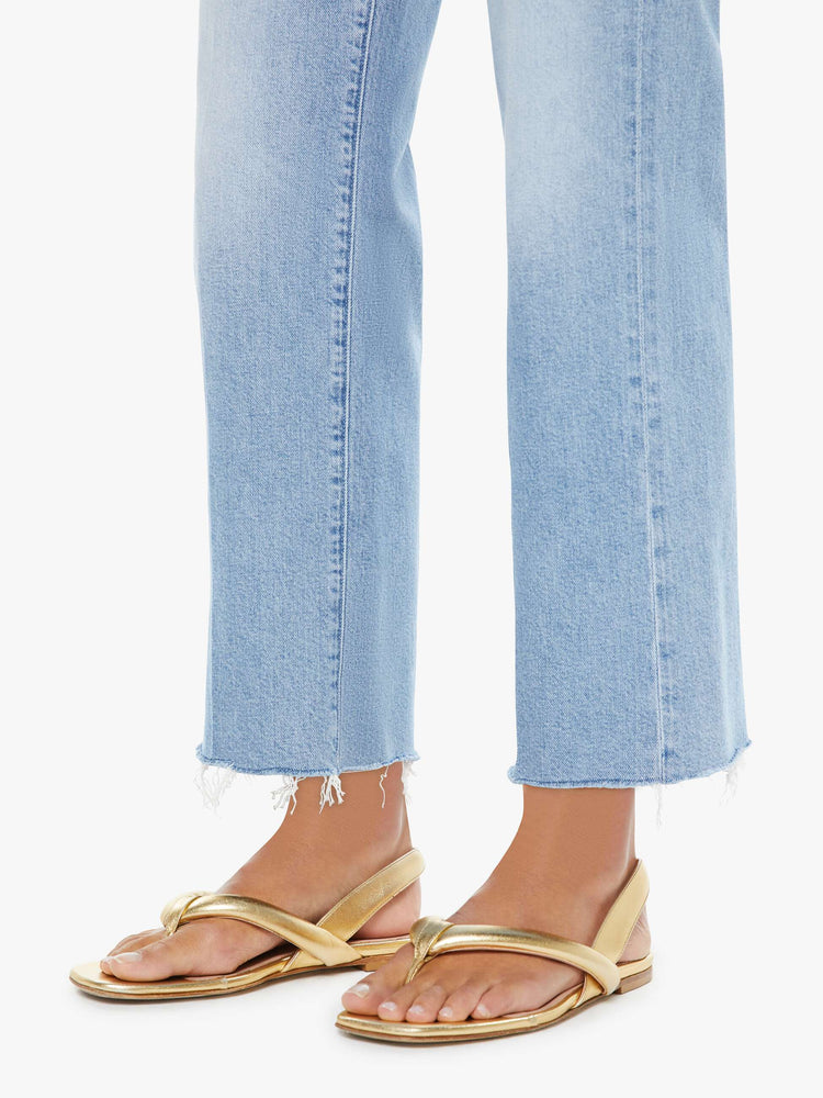 Hem view of a woman in a light blue mid-rise jeans with a wide straight leg, zip fly and an ankle-length inseam with a frayed hem.