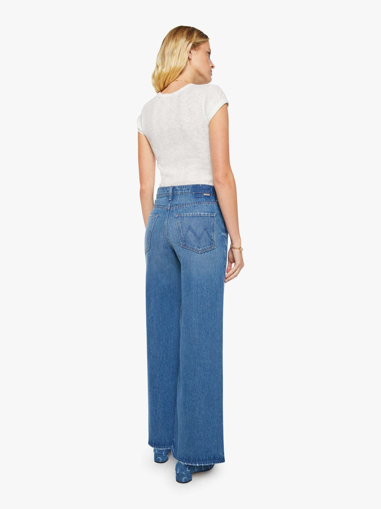 Back view of a woman in a med blue wide-leg jeans feature a high rise with a slightly dropped crotch, zip fly, low-set back pockets and a 32 1/4-inch inseam with a clean hem.