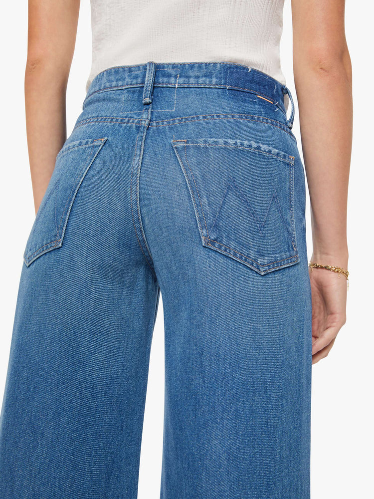 Close up view of a woman in a med blue wide-leg jeans feature a high rise with a slightly dropped crotch, zip fly, low-set back pockets and a 32 1/4-inch inseam with a clean hem.