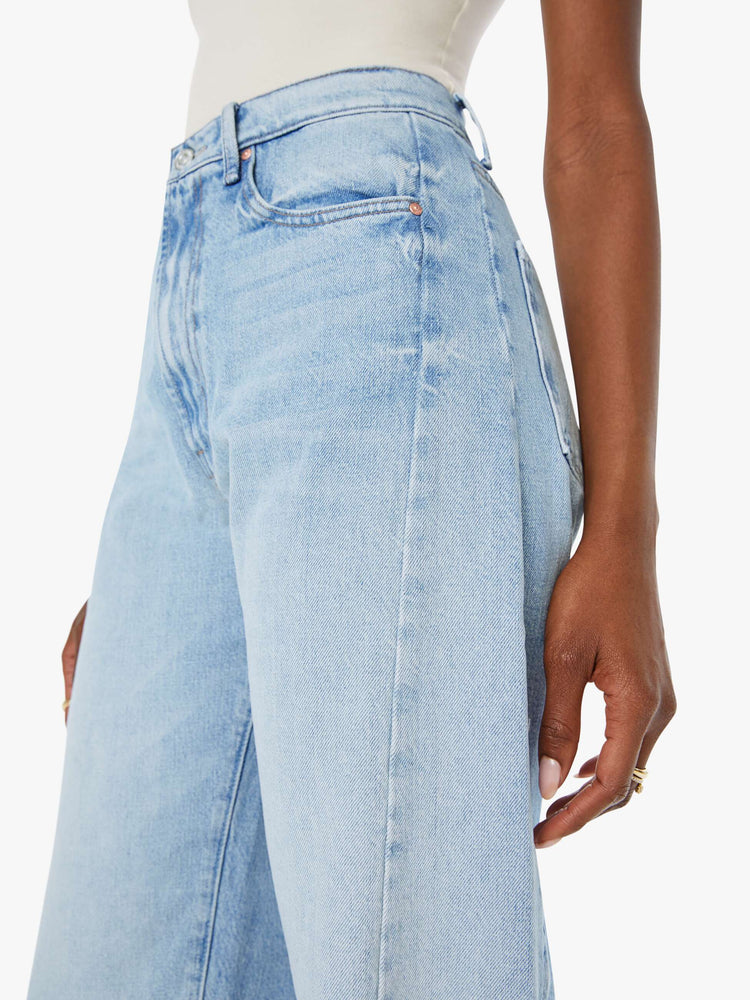 Side close up view of a woman super high-waisted jean with a wide, curved leg, an ankle-length inseam and a clean hem in a light blue wash.