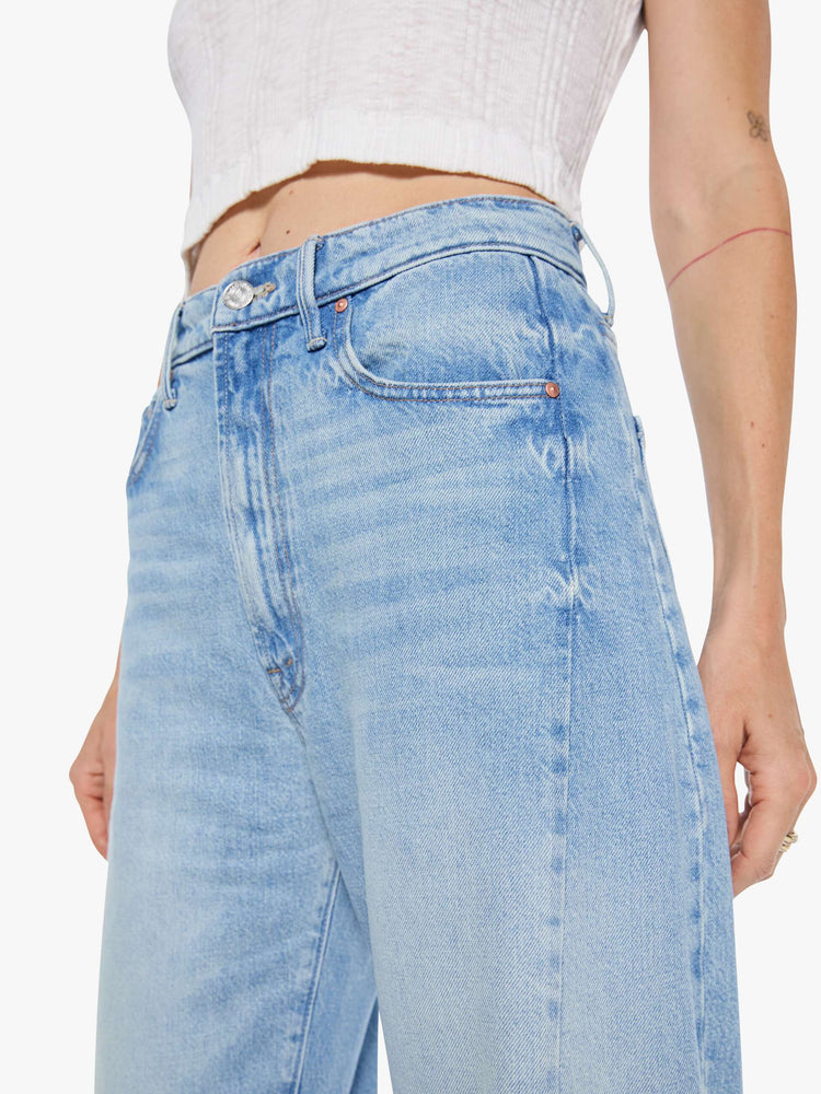 Side close up view of a woman super high-waisted jean with a wide, curved leg, an ankle-length inseam and a clean hem in a light blue wash.