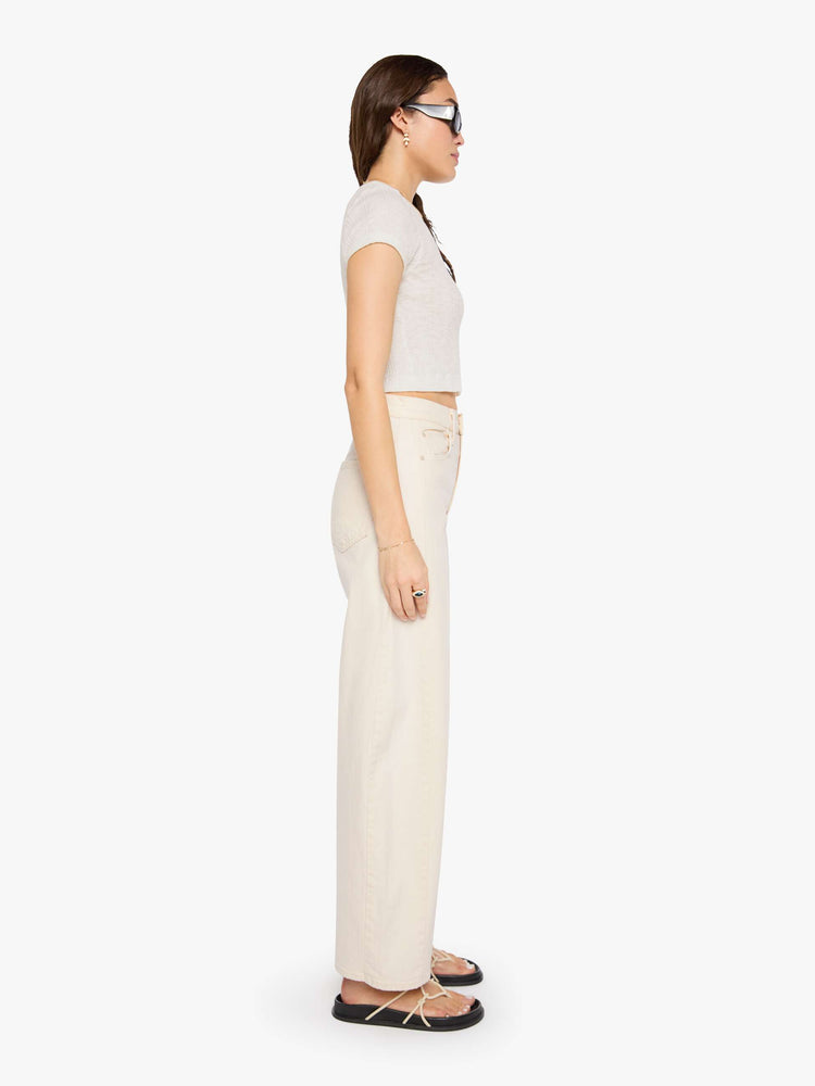 Side view of a woman in a cream white pant with super high-waisted jean with a wide, curved leg, an ankle-length inseam and a clean hem.