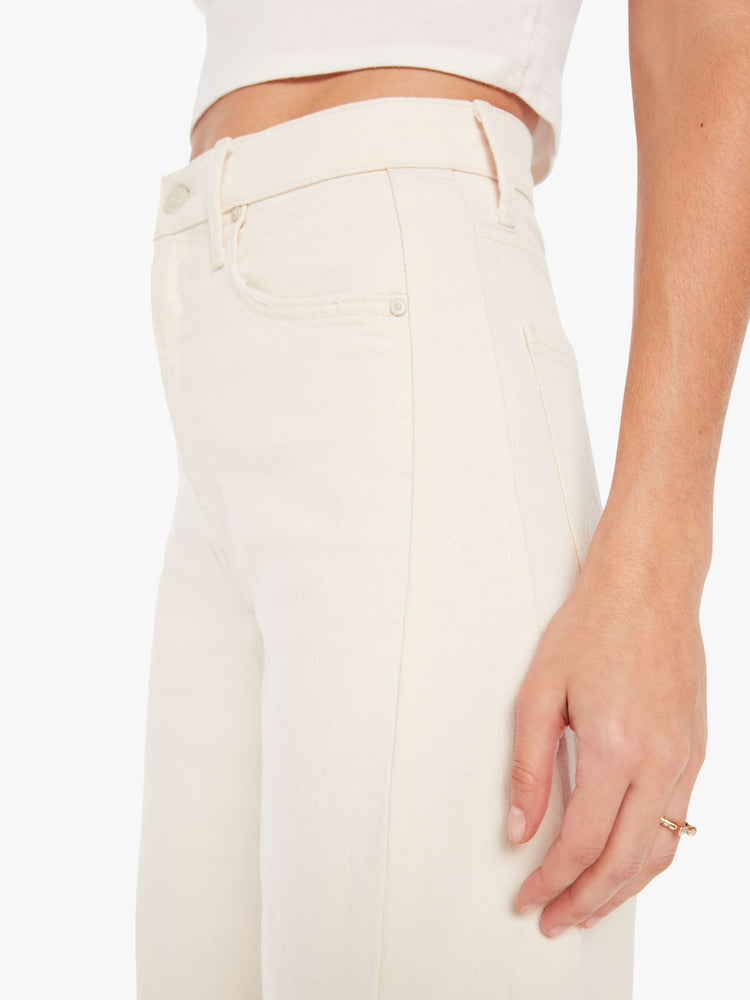 Waist close up view of a woman in a cream white pant with super high-waisted jean with a wide, curved leg, an ankle-length inseam and a clean hem.