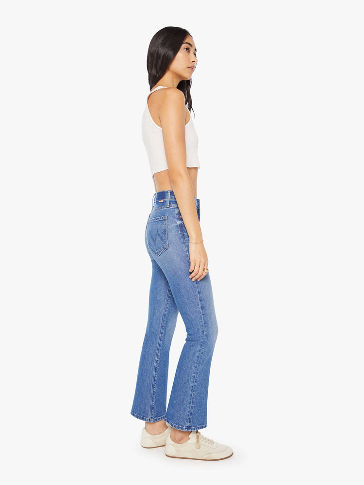 Side view of a woman in a med blue narrow flare jeans with a mid rise and a 28.25-inch inseam with a clean hem.