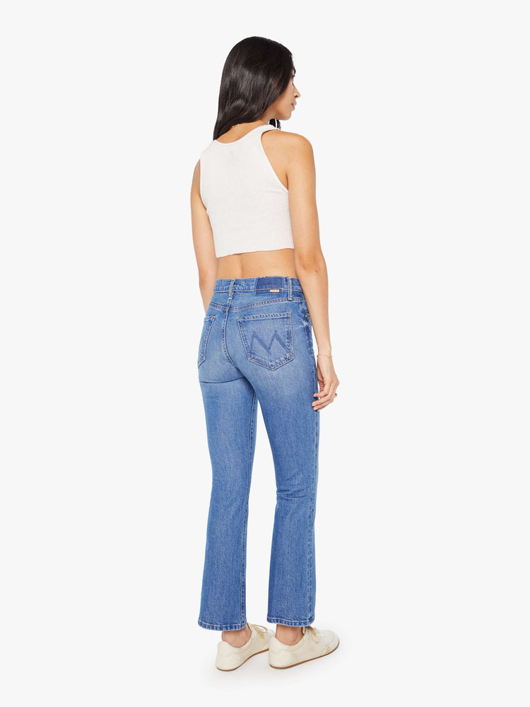 Back view of a woman in a med blue narrow flare jeans with a mid rise and a 28.25-inch inseam with a clean hem.