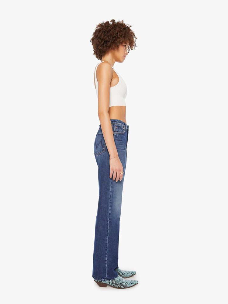 Side view of a woman in dark blue high-waisted jeans with a wide straight leg, zip fly, long 34-inch inseam and a clean hem.