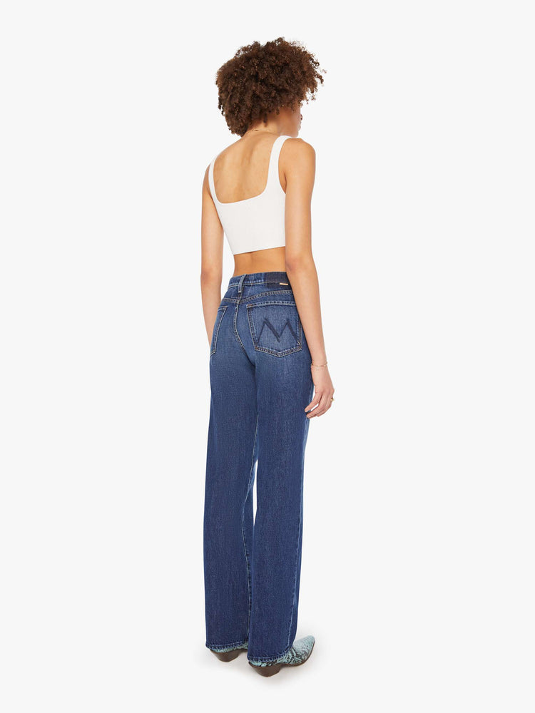 Back view of a woman in dark blue high-waisted jeans with a wide straight leg, zip fly, long 34-inch inseam and a clean hem.