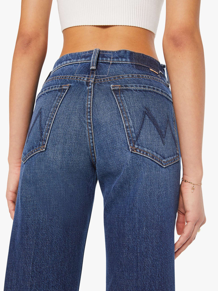 Waist back close up view of a woman in dark blue high-waisted jeans with a wide straight leg, zip fly, long 34-inch inseam and a clean hem.