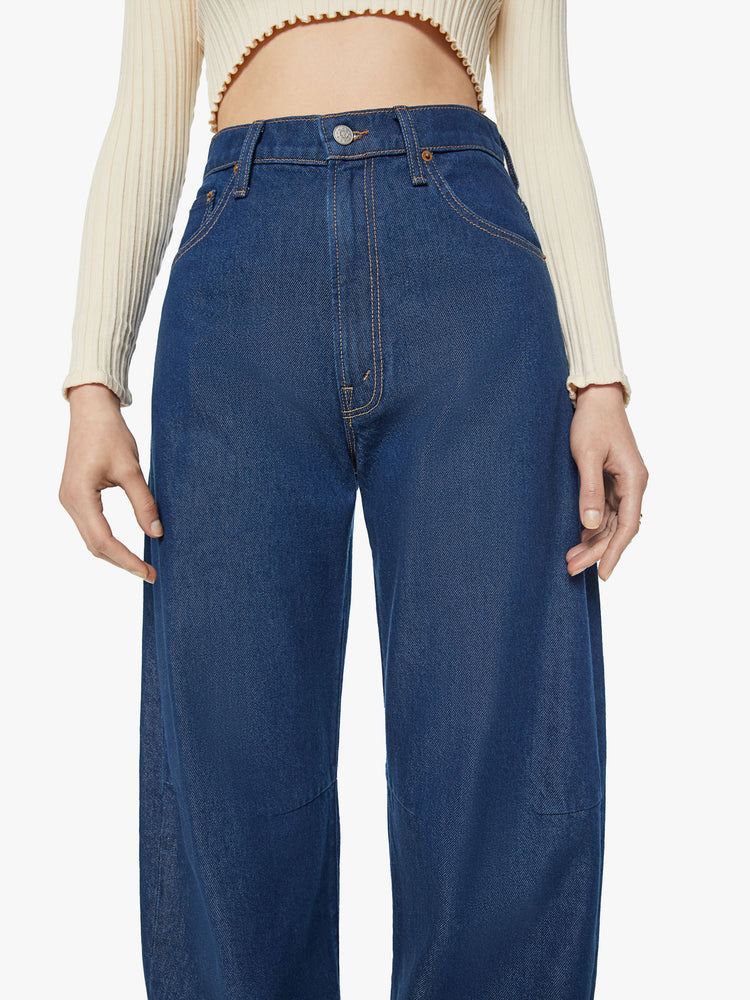 Close up view of a woman super high-rise jeans are designed with loose fit and a tapered leg with a long 34-inch inseam that stacks at the ankle in a dark blue wash.