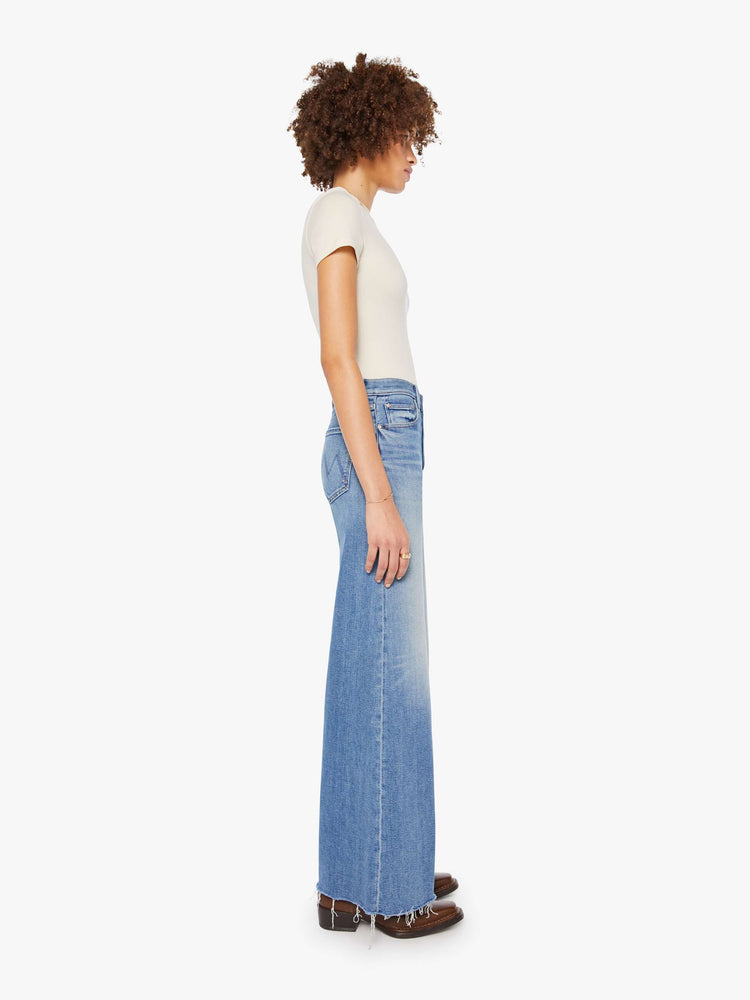 Side view of a woman in a med blue high-waisted wide-leg jeans with a button fly, long 32-inch inseam and a frayed hem.